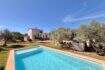 Außenansicht mediterrane Finca Algaida mit Pool, Olivenbäumen und rosa Haupthaus unter blauem Himmel.