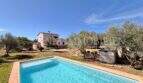 Außenansicht mediterrane Finca Algaida mit Pool, Olivenbäumen und rosa Haupthaus unter blauem Himmel.