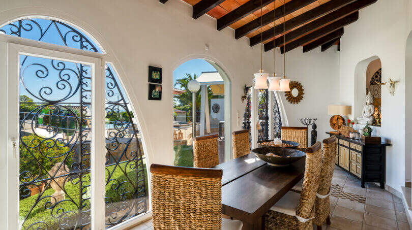 Mediterranean dining room of the sea view villa in Cala Murada with wooden beam ceiling, wicker chairs and wrought iron window.