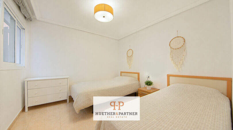 Helles Schlafzimmer der Erdgeschosswohnung Cala Antena mit zwei Einzelbetten, weißen Wänden und Traumfängern.