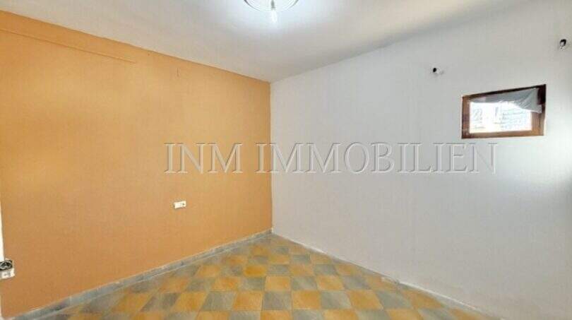 Empty room with orange accent wall, checkerboard floor and small window, apartment needing renovation Palma