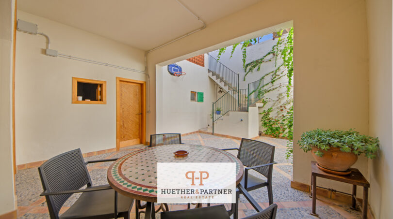 Überdachte Terrasse mit Mosaiktisch, schwarzen Stühlen und Blick auf begrünten Innenhof mit Treppe in Manacor