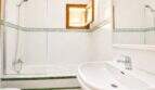 Helles Badezimmer der Finca mit weißen Fliesen, grünem Bordürenmuster, Badewanne mit Dusche und Waschbecken.