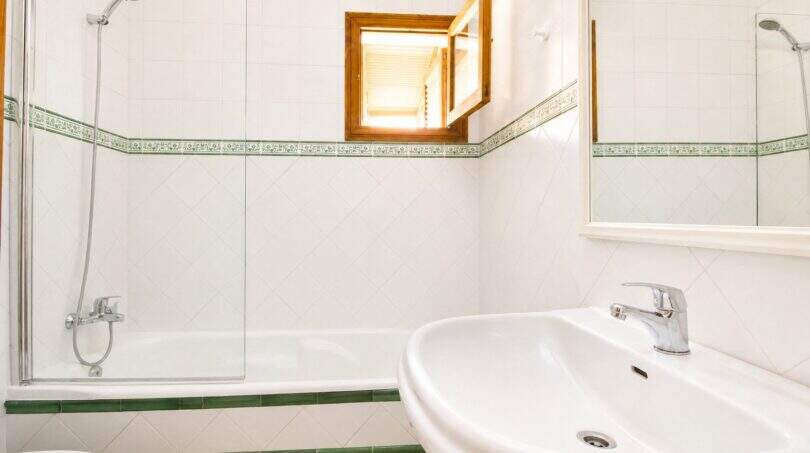 Helles Badezimmer der Finca mit weißen Fliesen, grünem Bordürenmuster, Badewanne mit Dusche und Waschbecken.