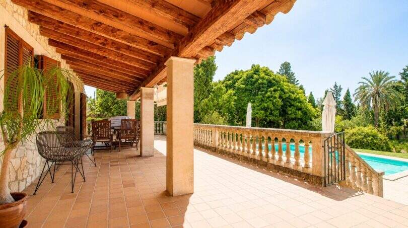 Überdachte Terrasse der Finca mit Holzbalkendecke, Sitzbereich und Blick auf den Pool und üppigen Garten.
