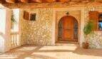 Eingangsbereich der Finca mit Natursteinwand, gewölbter Holztür und rustikalen Holzbalken in Palma de Mallorca.