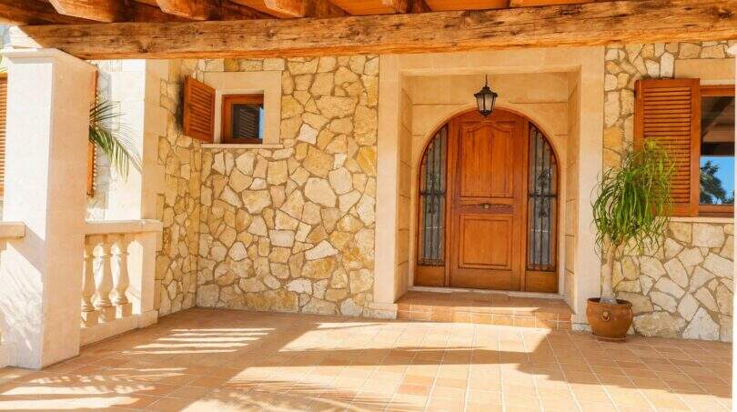 Eingangsbereich der Finca mit Natursteinwand, gewölbter Holztür und rustikalen Holzbalken in Palma de Mallorca.