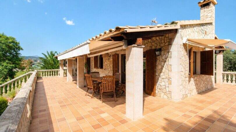 Sonnige Terrasse der Finca in Palma mit Natursteinwänden, Terrakottafliesen und Holzmöbeln unter Markise