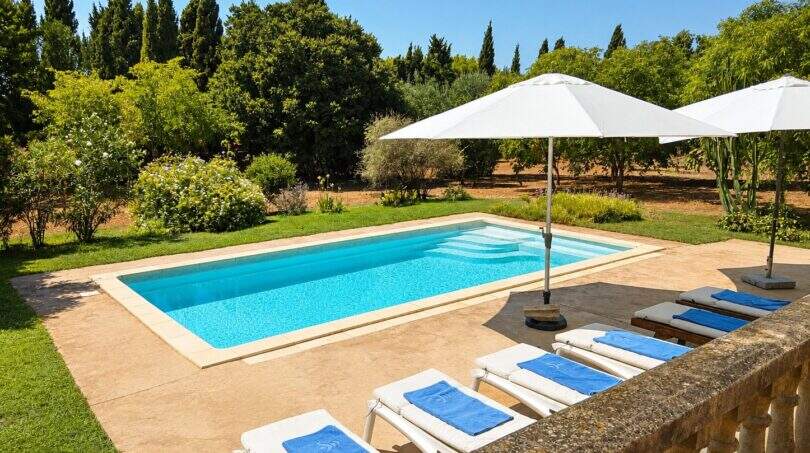 Finca Mallorca: Rechteckiger Außenpool mit Liegestühlen, Sonnenschirmen und gepflegtem Garten mit Zypressen