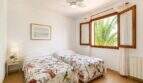 Helles Schlafzimmer der Finca Mallorca mit zwei Einzelbetten, Blumendecken, Deckenventilator und Palmenblick durchs Holzfenster.