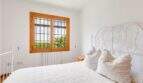 Helles Schlafzimmer der Finca mit weißem Schmiedeeisenbett, Holzfenster und Gartenblick in Palma de Mallorca.