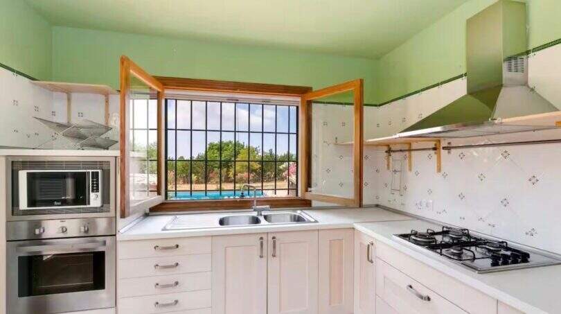 Helle Küche mit weißen Schränken, Gasherd, Einbauofen und Fenster mit Blick auf Pool der Finca in Mallorca