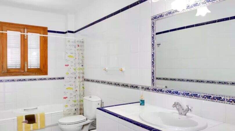 Helles Badezimmer der Finca mit weißen Kacheln, blau-weißem Fliesenbord, Badewanne und großem Spiegel.