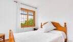 Helles Schlafzimmer der Finca mit Doppelbett, Holzmöbeln und Fenster mit Gartenblick.