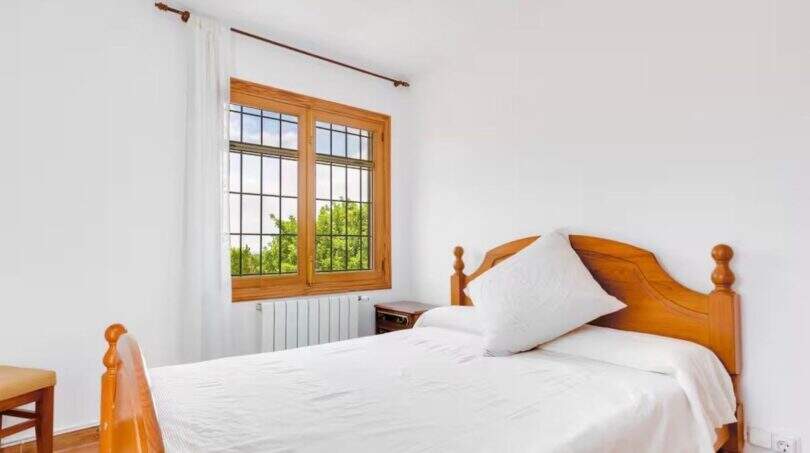 Helles Schlafzimmer der Finca mit Doppelbett, Holzmöbeln und Fenster mit Gartenblick.