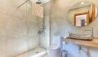 Modernes Badezimmer der Finca mit Glasdusche, Naturstein-Waschbecken, WC und rundem Spiegel