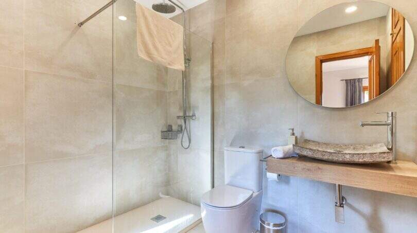 Modernes Badezimmer der Finca mit Glasdusche, Naturstein-Waschbecken, WC und rundem Spiegel