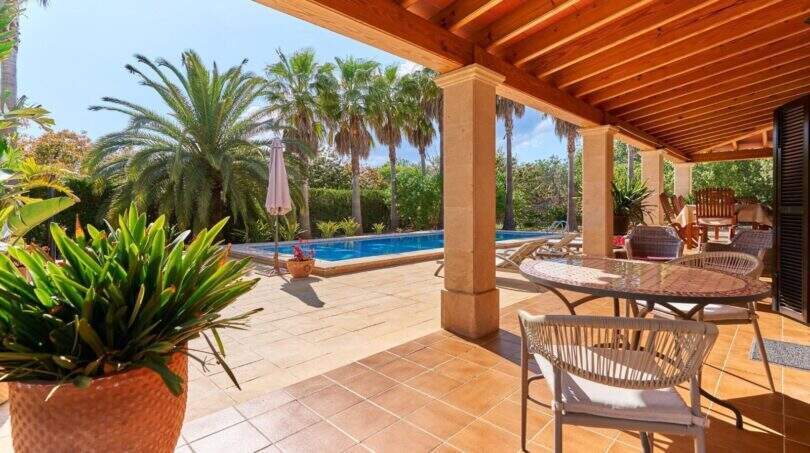 Überdachte Terrasse der Finca mit Holzdecke, Sitzbereich und Pool umgeben von Palmen in Palma de Mallorca