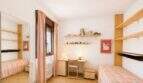 Helles Kinderzimmer mit zwei Einzelbetten, Schreibtisch, Holzregalen und rosa Streifenbettwäsche in Palma-Wohnung.