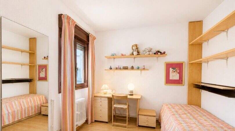 Helles Kinderzimmer mit zwei Einzelbetten, Schreibtisch, Holzregalen und rosa Streifenbettwäsche in Palma-Wohnung.