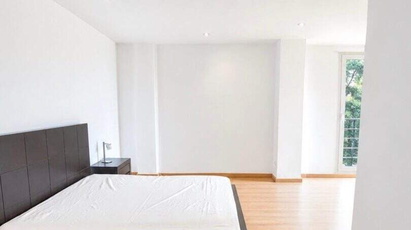 Helles Schlafzimmer mit Parkettboden, dunklem Doppelbett und großem Fenster mit Grünblick