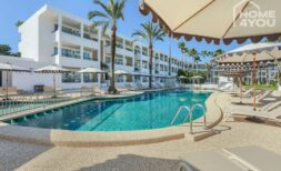 Hotelpool mit Liegestühlen und Sonnenschirmen, weiße Fassade mit Balkonen und Palmen in Portocolom