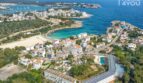 Vista aérea del apartamento hotel Portocolom: edificios blancos, piscina, bahía azul turquesa, Mediterráneo de fondo.