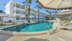 Piscina del hotel con tumbonas y sombrillas, edificio hotelero blanco con balcones y palmeras en Portocolom