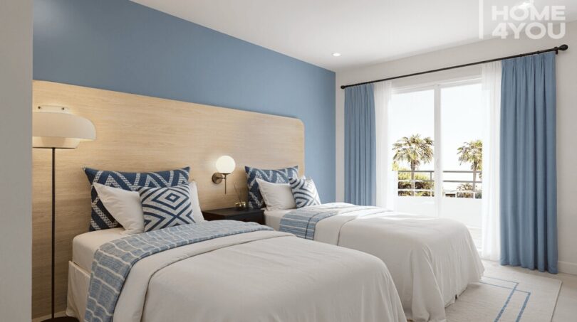 Dormitorio luminoso con dos camas, pared de acento azul y vistas al mar en el apartahotel Portocolom