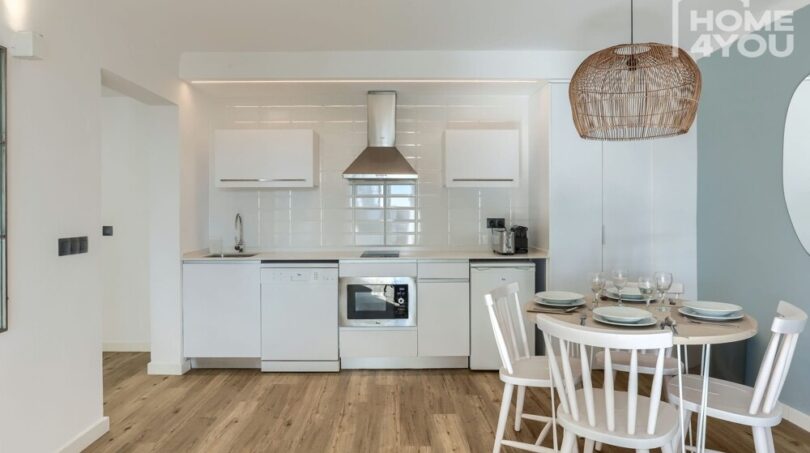 Apartamento moderno en Portocolom: cocina abierta con electrodomésticos blancos y área de comedor con lámpara de ratán