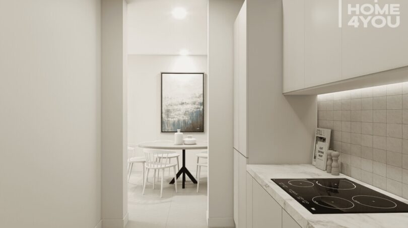 Cocina blanca moderna con placa de cerámica y encimera de mármol, vista del área de comedor luminosa en el apartahotel Portocolom