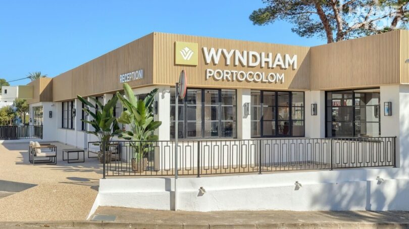 Vista exterior del Hotel Wyndham Portocolom con fachada moderna de madera, recepción y plantas tropicales, Mallorca