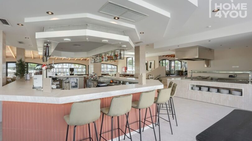 Restaurante hotelero moderno con mostrador, taburetes de bar y cocina abierta en hotel de inversión Portocolom