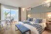 Habitación de hotel luminosa con dos camas, decoración azul, aire acondicionado y balcón con vista al mar en Portocolom
