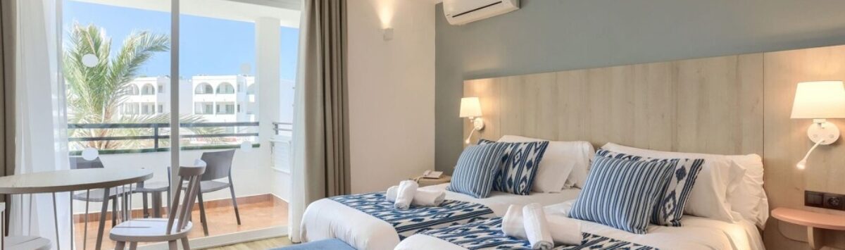 Habitación de hotel luminosa con dos camas, decoración azul, aire acondicionado y balcón con vista al mar en Portocolom