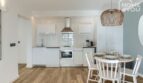 Apartamento luminoso en Portocolom: cocina abierta con frentes blancos, mesa de comedor para 4 personas, suelo de madera
