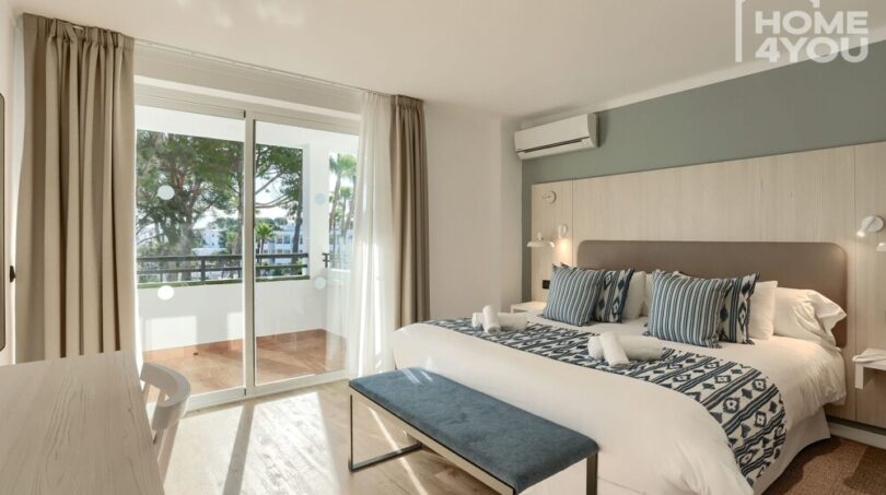 Dormitorio luminoso con cama doble, balcón, aire acondicionado y suelo de madera en el apartahotel Portocolom