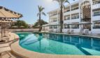 Complejo hotelero en Portocolom con piscina curva, tumbonas, sombrillas y fachada blanca con balcones