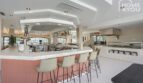 Restaurante hotelero con bar elegante, mostrador rosa, taburetes de bar y cocina abierta en Portocolom