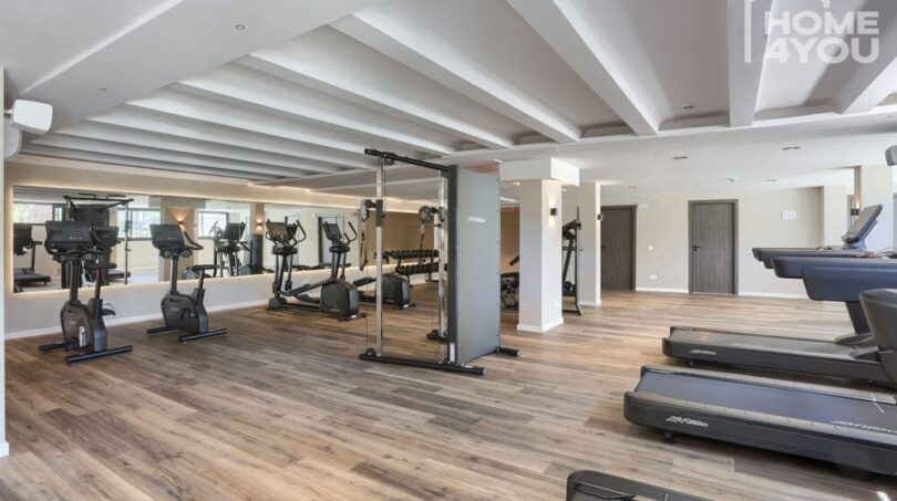 Centro de fitness moderno con cintas de correr, bicicletas estáticas y máquinas elípticas, suelo de madera, pared espejo en el apartahotel Portocolom