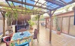 Terraza cubierta con pérgola de madera, mesa de comedor, plantas y zona lounge del apartamento en Palma-City.