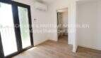 Dormitorio claro con suelo de madera, aire acondicionado, acceso al balcón y baño adyacente en apartamento esquinero de nueva construcción Cala Millor