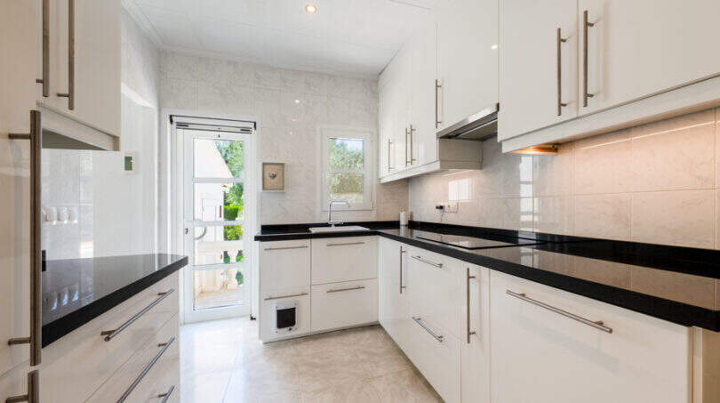 Moderne weiße Küche mit schwarzen Granitarbeitsflächen und Glastür zum Garten in Villa Cala Murada