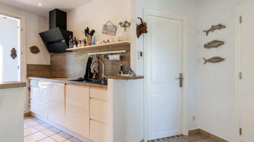 Modern kitchen of the sea view villa in Cala Murada with white fronts, wooden worktop and black extractor hood.