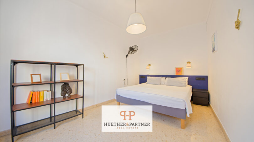 Helles Schlafzimmer mit Doppelbett, blauem Kopfteil, Bücherregal und Deckenlampe im Stadthaus Manacor
