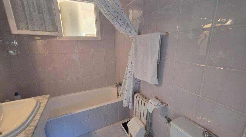 Bathroom of the finca in Cala Millor with bathtub, shower curtain, radiator and tiled walls