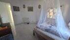 Bright bedroom of the finca with mosquito net four-poster bed, tile floor and white walls