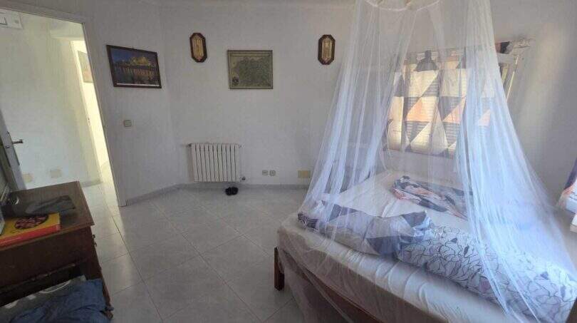 Bright bedroom of the finca with mosquito net four-poster bed, tile floor and white walls
