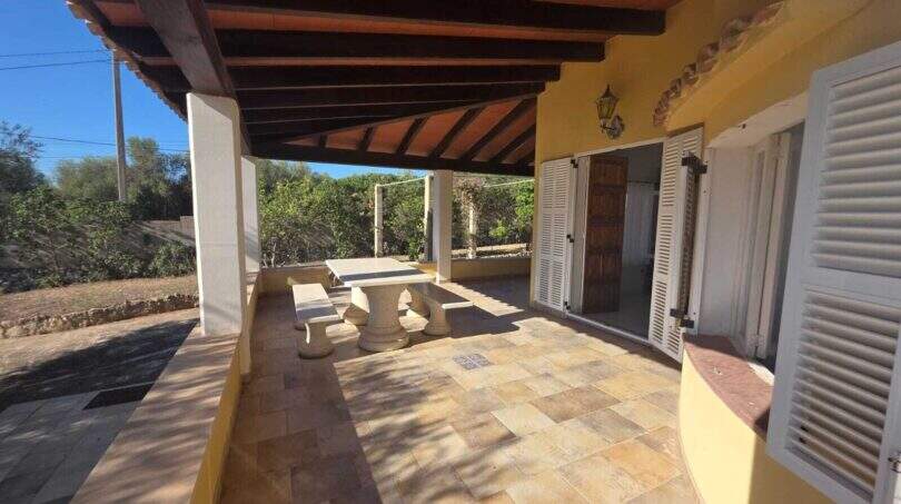 Covered terrace of the finca in Cala Millor with wooden beam ceiling, natural stone furniture and garden view