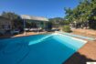 Outdoor pool of the finca in Cala Millor with sun terrace, pergola and lush greenery under blue sky.